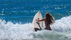 a woman standing in the ocean with her surfboard looking at the waves behind her