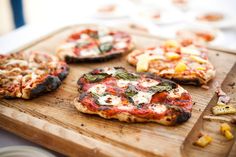 several small pizzas on a wooden cutting board