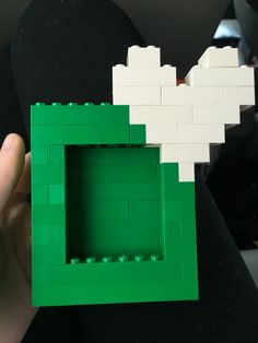 someone is holding up a small green and white lego block