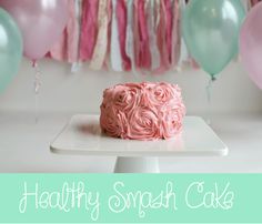 a pink frosted cake sitting on top of a white plate next to balloons and streamers