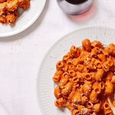 two white plates with pasta and sauce on them next to a cup of coffee, fork and spoon