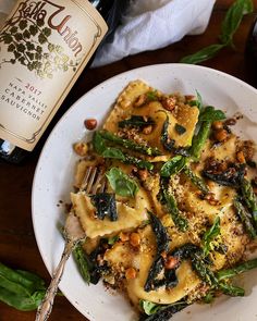 a white plate topped with pasta covered in sauce and vegetables next to a bottle of wine