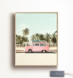 a pink van parked in front of palm trees with a surfboard on the roof