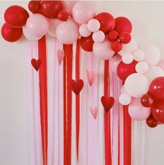 balloons and streamers are hanging from the ceiling in front of a wall with hearts