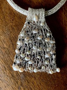 a white netted bag with pearls hanging from it's side on a wooden table