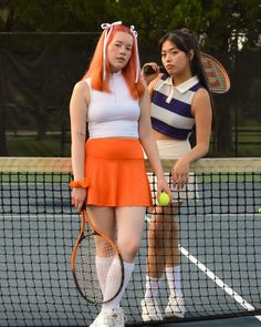 two young women standing on a tennis court holding racquets and tennis balls