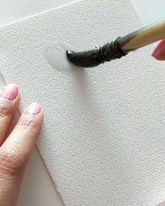 a woman is using a brush to paint a piece of paper