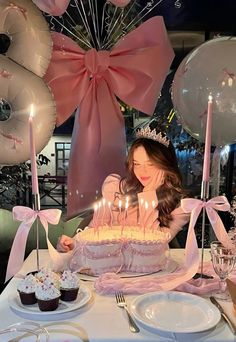 a woman sitting at a table with a cake and cupcakes in front of her