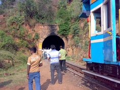 three men are walking towards a train that is going into a tunnel on the tracks