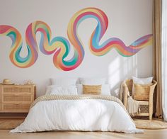 a white bed sitting under a colorful wall mural