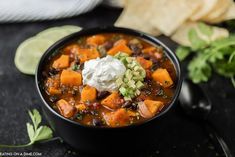 a black bowl filled with chili and sweet potato soup next to tortilla chips