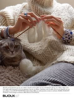 a woman is knitting while her cat looks on