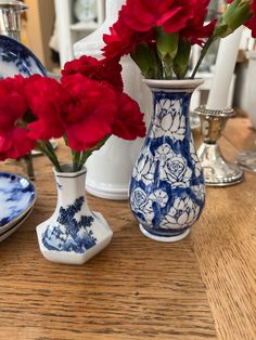 red flowers in blue and white vases sitting on a wooden table next to plates