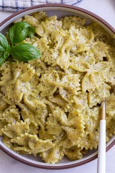 a white bowl filled with pasta and pesto on top of a table next to a spoon