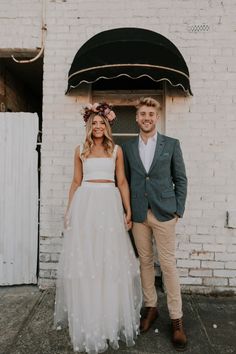 a man and woman standing next to each other in front of a white brick building