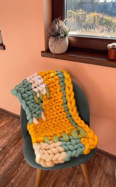 a knitted blanket sitting on top of a green chair in front of a window