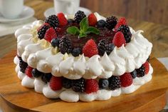 a cake with berries and whipped cream is on a wooden platter next to a cup of coffee