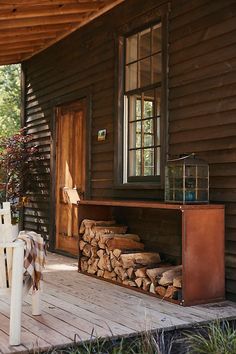 a house with wood stacked on top of it's porch and a table next to the firewood