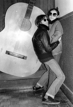 two people standing next to each other in front of an acoustic guitar and wearing sunglasses