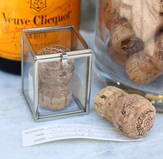 two wine corks in a glass container next to a bottle of wine and paper