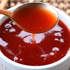 a spoon full of sauce being poured into a white bowl on top of a table