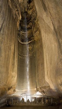 the inside of a cave with water coming from it's ceiling and people standing on either side