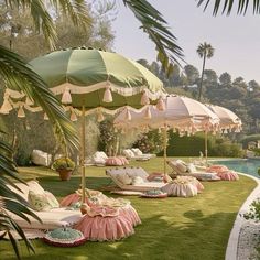 some lawn chairs and umbrellas in the grass near a swimming pool with palm trees