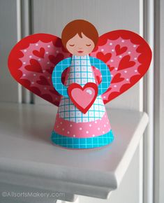 a paper angel holding a heart on top of a table