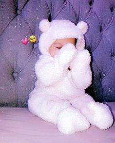 a baby wrapped in a white teddy bear costume sitting on a couch with its eyes closed