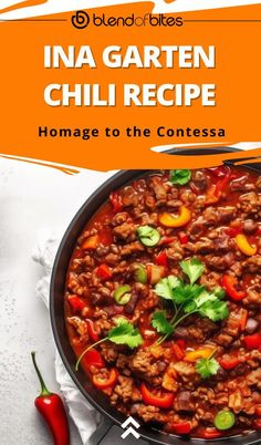 a skillet filled with chili and meat on top of a white table next to a red pepper