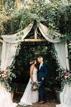 a bride and groom standing under an outdoor wedding ceremony arch with greenery on either side