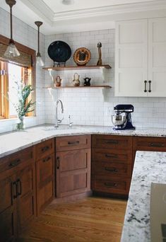 a kitchen with wooden cabinets and marble counter tops, white subway tile backsplash