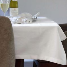 two bottles of wine are sitting on a dining room table with white linens and silverware