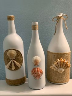 three wine bottles decorated with seashells and burlocks are sitting on a shelf