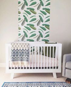 a white crib in front of a wall with green leaves on it and a blue rug