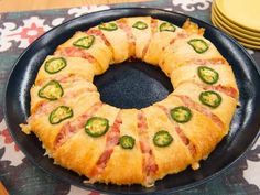 a black plate topped with a pastry covered in bacon and jalapeno slices