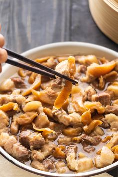 a person holding chopsticks over a bowl of food with meat and vegetables in it