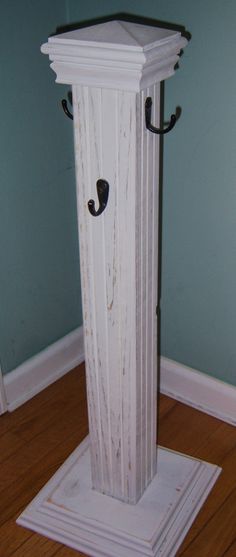 a white pedestal with two black hooks on it's sides and a wooden floor