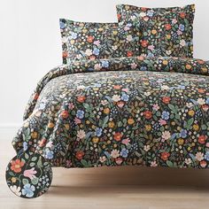 a bed covered in a black floral comforter and matching pillowcases with pillows