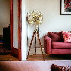 a living room with a red couch and an old fashioned fan on a tripod