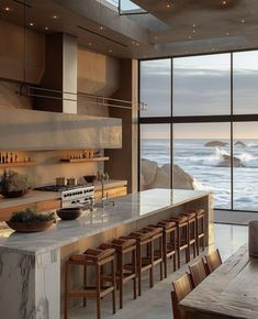 a large kitchen with an island counter and wooden chairs in front of the window overlooking the ocean