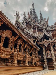 an elaborately carved wooden building with statues on the roof and side walls, under a cloudy blue sky