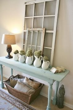 a blue table topped with vases filled with flowers next to a mirror and lamp