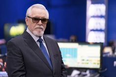 an older man in a suit and sunglasses standing next to a computer monitor on a desk