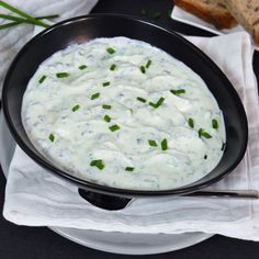 a black bowl filled with white sauce on top of a table next to some bread