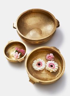 three metal bowls with flowers in them on a white surface and one bowl is empty