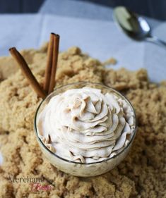 a glass bowl filled with whipped cream and cinnamon sticks on top of a white table cloth