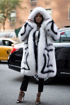 a woman wearing a white and black fur coat on the street with cars in the background