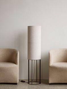 two chairs and a lamp on the floor in front of a wall with white walls