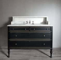 a black and white bathroom vanity with marble counter top, two faucets on legs